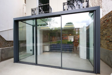 This is an example of a small contemporary conservatory in London with limestone flooring and a glass ceiling.