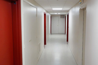 Cette image montre un très grand couloir minimaliste avec un mur blanc, un sol en carrelage de céramique et un sol blanc.