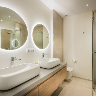 Foto de cuarto de baño con ducha, actual, con armarios con paneles lisos, puertas de armario de madera clara, ducha esquinera, sanitario de pared, baldosas y/o azulejos beige, paredes blancas, lavabo sobreencimera, suelo beige y encimeras grises