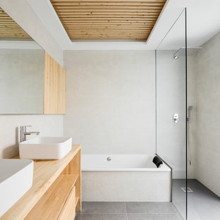 Foto de cuarto de baño minimalista con armarios abiertos, baldosas y/o azulejos grises, baldosas y/o azulejos beige, puertas de armario de madera clara, bañera encastrada, ducha a ras de suelo, baldosas y/o azulejos en mosaico, paredes blancas, lavabo sobreencimera, encimera de madera, suelo gris, ducha abierta y encimeras beige