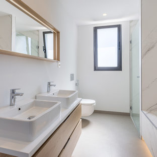 Modelo de cuarto de baño con ducha, actual, de tamaño medio, sin sin inodoro, con puertas de armario de madera clara, sanitario de pared, baldosas y/o azulejos blancos, baldosas y/o azulejos de cerámica, paredes blancas, suelo de baldosas de cerámica, lavabo sobreencimera, encimera de madera, ducha con puerta con bisagras, encimeras blancas, armarios con paneles lisos, bañera encastrada sin remate y suelo beige