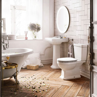 Foto de cuarto de baño de estilo de casa de campo con puertas de armario blancas, bañera con patas, sanitario de dos piezas, baldosas y/o azulejos beige, paredes blancas, suelo de madera en tonos medios, lavabo con pedestal, suelo beige y encimeras blancas