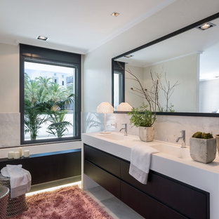 Ejemplo de cuarto de baño contemporáneo con armarios con paneles lisos, puertas de armario negras, bañera encastrada sin remate, baldosas y/o azulejos grises, paredes blancas, lavabo integrado, suelo gris y encimeras blancas