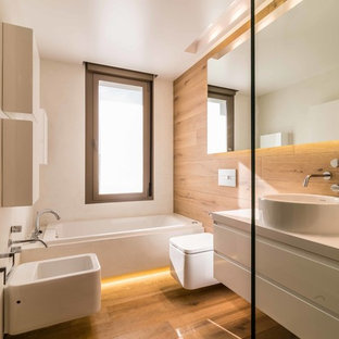 Modern inredning av ett mellanstort en-suite badrum, med ett fristående handfat, släta luckor, vita skåp, en bidé, mellanmörkt trägolv, bänkskiva i akrylsten, flerfärgade väggar och ett platsbyggt badkar