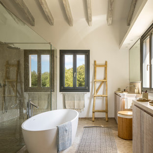 Diseño de cuarto de baño principal, mediterráneo, con armarios con paneles lisos, puertas de armario de madera clara, bañera exenta, ducha a ras de suelo, baldosas y/o azulejos grises, paredes blancas, suelo marrón, ducha con puerta con bisagras y encimeras beige