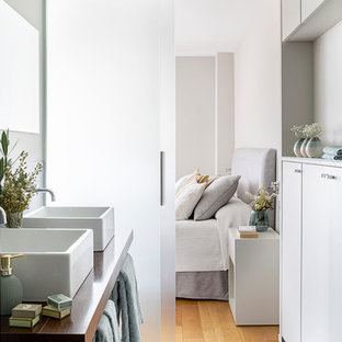 Modelo de cuarto de baño principal, actual, con armarios con paneles lisos, puertas de armario blancas, paredes grises, lavabo sobreencimera, encimera de madera, suelo gris y encimeras marrones
