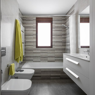 Foto di una piccola stanza da bagno minimal con ante lisce, ante bianche, vasca/doccia, WC sospeso, piastrelle a mosaico, pareti multicolore, pavimento in ardesia, lavabo integrato, top in superficie solida, piastrelle grigie e vasca da incasso