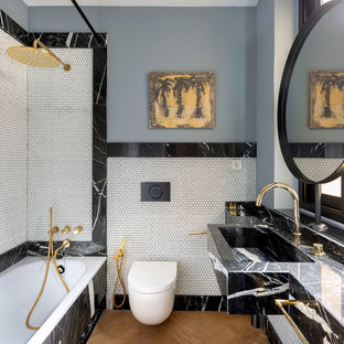 Modelo de cuarto de baño con ducha, contemporáneo, con bañera encastrada, combinación de ducha y bañera, sanitario de pared, baldosas y/o azulejos blancas y negros, baldosas y/o azulejos blancos, baldosas y/o azulejos en mosaico, paredes grises, suelo de madera en tonos medios, lavabo integrado, encimera de mármol, suelo marrón, ducha con cortina y encimeras negras