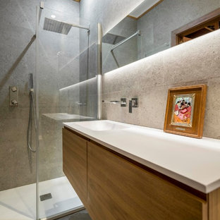 Diseño de cuarto de baño con ducha, actual, de tamaño medio, con armarios con paneles lisos, puertas de armario de madera oscura, ducha empotrada, lavabo integrado, baldosas y/o azulejos grises, paredes grises, suelo gris y encimeras blancas