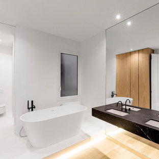 Modelo de cuarto de baño principal, minimalista, con bañera exenta, encimeras negras, paredes blancas y lavabo bajoencimera