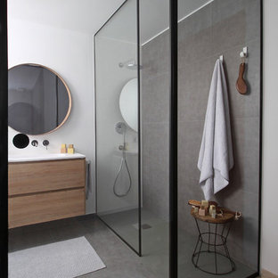 Imagen de cuarto de baño principal, moderno, de tamaño medio, con armarios con paneles lisos, puertas de armario de madera oscura, ducha abierta, sanitario de pared, baldosas y/o azulejos grises, paredes blancas, suelo gris, encimeras blancas y lavabo tipo consola