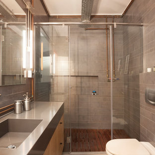 Imagen de cuarto de baño con ducha, industrial, con armarios con paneles lisos, puertas de armario de madera clara, ducha empotrada, sanitario de una pieza, baldosas y/o azulejos grises, lavabo integrado, encimera de acero inoxidable, ducha con puerta corredera y encimeras grises