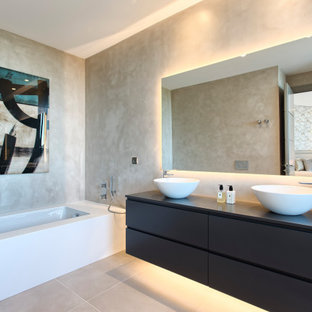 Modelo de cuarto de baño doble, contemporáneo, con armarios con paneles lisos, puertas de armario negras, bañera encastrada sin remate, paredes beige, lavabo sobreencimera y suelo gris