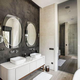 Foto de cuarto de baño principal, doble y de pie, contemporáneo, con armarios con paneles lisos, puertas de armario grises, paredes negras, suelo de madera clara, lavabo sobreencimera y encimeras blancas