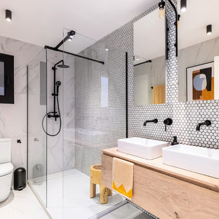 Imagen de cuarto de baño principal, actual, de tamaño medio, con armarios con paneles lisos, puertas de armario de madera clara, ducha abierta, baldosas y/o azulejos blancos, baldosas y/o azulejos en mosaico, lavabo sobreencimera, encimera de madera, suelo gris, ducha abierta y encimeras beige