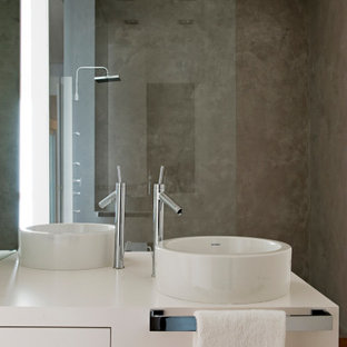 Modelo de cuarto de baño industrial con armarios con paneles lisos, puertas de armario blancas, paredes grises, suelo de madera en tonos medios, lavabo sobreencimera y suelo marrón
