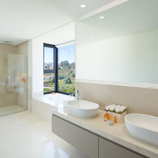 Modelo de cuarto de baño principal, contemporáneo, con armarios con paneles lisos, ducha a ras de suelo, baldosas y/o azulejos beige, paredes beige, lavabo sobreencimera, encimeras beige, puertas de armario beige, bañera encastrada, suelo beige y ducha abierta