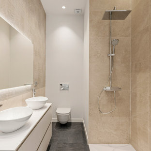 Modelo de cuarto de baño con ducha, actual, grande, con armarios con paneles lisos, puertas de armario blancas, ducha esquinera, sanitario de pared, baldosas y/o azulejos beige, baldosas y/o azulejos de porcelana, paredes blancas, lavabo sobreencimera, suelo gris, ducha abierta y encimeras blancas