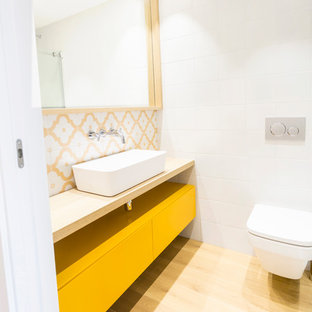 Ejemplo de cuarto de baño nórdico con puertas de armario amarillas, paredes blancas, encimera de madera, armarios con paneles lisos, sanitario de pared, baldosas y/o azulejos multicolor, baldosas y/o azulejos blancos, baldosas y/o azulejos amarillos, suelo de madera clara y lavabo sobreencimera