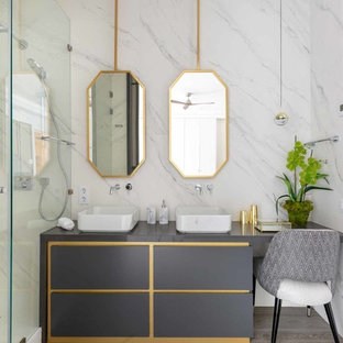 Modelo de cuarto de baño con ducha, actual, con armarios tipo mueble, puertas de armario grises, ducha empotrada, baldosas y/o azulejos blancos, paredes blancas, lavabo sobreencimera, ducha con puerta con bisagras y encimeras grises