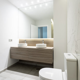Foto de cuarto de baño con ducha, actual, de tamaño medio, con armarios con paneles lisos, puertas de armario beige, sanitario de una pieza, baldosas y/o azulejos blancos, baldosas y/o azulejos de porcelana, paredes blancas, lavabo sobreencimera, encimera de madera, suelo gris y encimeras beige
