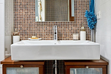 Cette image montre une salle de bain traditionnelle avec des portes de placard marrons, un carrelage marron, mosaïque, un mur blanc et un lavabo intégré.