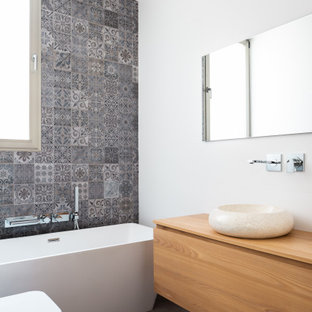 Foto de cuarto de baño con ducha, actual, de tamaño medio, con armarios con paneles lisos, puertas de armario de madera oscura, bañera exenta, sanitario de pared, baldosas y/o azulejos grises, paredes blancas, lavabo sobreencimera, encimera de madera, suelo gris y encimeras beige