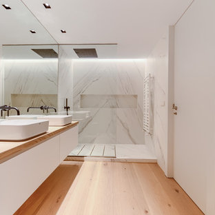 Ejemplo de cuarto de baño principal, actual, de tamaño medio, con armarios con paneles lisos, puertas de armario blancas, ducha abierta, baldosas y/o azulejos blancos, baldosas y/o azulejos de mármol, paredes blancas, lavabo sobreencimera, encimera de madera, suelo marrón, suelo de madera clara, ducha abierta y encimeras marrones
