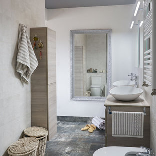 Modelo de cuarto de baño doble, con ducha y a medida, contemporáneo, de tamaño medio, con puertas de armario de madera clara, sanitario de pared, baldosas y/o azulejos beige, paredes blancas, lavabo sobreencimera, encimera de madera, suelo gris y encimeras beige