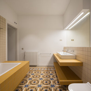Ejemplo de cuarto de baño con ducha, mediterráneo, con puertas de armario amarillas, bañera encastrada, sanitario de pared, baldosas y/o azulejos beige, baldosas y/o azulejos de cemento, paredes blancas, lavabo de seno grande, suelo multicolor y encimeras amarillas