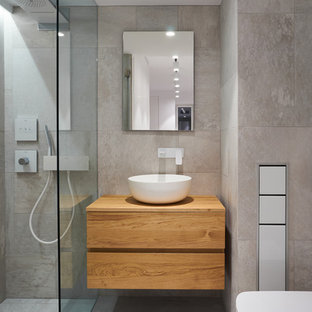 Ejemplo de cuarto de baño con ducha, contemporáneo, con armarios tipo mueble, puertas de armario de madera oscura, ducha a ras de suelo, baldosas y/o azulejos grises, paredes grises, lavabo sobreencimera y encimera de madera