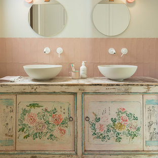 Imagen de cuarto de baño infantil, romántico, de tamaño medio, con armarios tipo mueble, suelo de madera en tonos medios, lavabo sobreencimera, encimera de madera, puertas de armario con efecto envejecido, baldosas y/o azulejos rosa y paredes beige