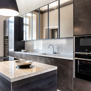 Idee per una cucina parallela design con lavello integrato, ante marroni, paraspruzzi beige, elettrodomestici neri, isola e top beige