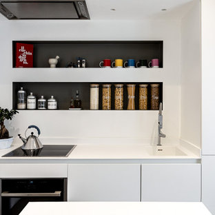 Ispirazione per una piccola cucina minimal con lavello integrato, ante lisce, ante bianche, top in superficie solida, paraspruzzi bianco, elettrodomestici da incasso, pavimento in gres porcellanato, penisola, pavimento grigio e top bianco