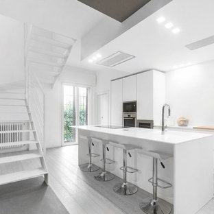 Esempio di una cucina parallela minimal con ante lisce, ante bianche, elettrodomestici in acciaio inossidabile, isola, pavimento grigio e top bianco