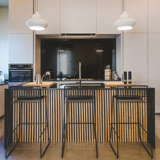 Idee per una cucina contemporanea con lavello sottopiano, ante lisce, ante bianche, paraspruzzi nero, paraspruzzi in lastra di pietra, elettrodomestici in acciaio inossidabile, pavimento in cemento, pavimento grigio e top nero