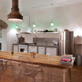 Modelo de cocina comedor lineal, urbana, sin isla, con armarios estilo shaker, puertas de armario blancas, encimera de cemento y suelo de madera en tonos medios