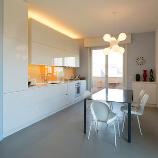 Ispirazione per una cucina minimal con lavello sottopiano, ante lisce, ante bianche, paraspruzzi arancione, paraspruzzi con lastra di vetro, elettrodomestici da incasso, pavimento in cemento, nessuna isola, pavimento grigio e top bianco