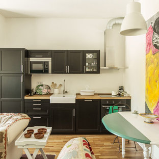 Ispirazione per una cucina bohémian di medie dimensioni con ante con bugna sagomata, ante nere, top in legno, paraspruzzi bianco, elettrodomestici neri, pavimento in legno massello medio, nessuna isola, pavimento marrone e lavello stile country
