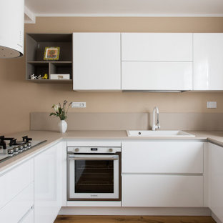 Foto di una cucina ad U design con lavello da incasso, ante lisce, ante bianche, elettrodomestici bianchi, pavimento in legno massello medio, penisola, pavimento marrone e top beige