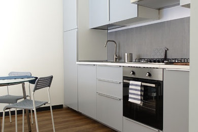 Foto på ett avskilt, mellanstort funkis grå linjärt kök, med en nedsänkt diskho, släta luckor, grå skåp, laminatbänkskiva, grått stänkskydd, stänkskydd i porslinskakel, laminatgolv, integrerade vitvaror och brunt golv