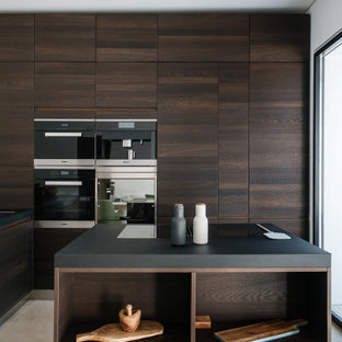 Foto di un cucina con isola centrale moderno con lavello a vasca singola, ante lisce, ante in legno bruno, elettrodomestici in acciaio inossidabile, pavimento grigio e top nero