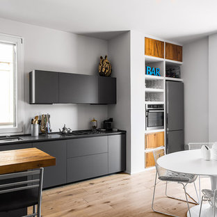 Ispirazione per una grande cucina abitabile nordica con ante lisce, elettrodomestici in acciaio inossidabile, parquet chiaro, lavello sottopiano, ante nere, pavimento beige e top nero