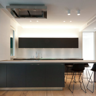 Idee per una cucina moderna con top in acciaio inossidabile, ante lisce, ante nere, penisola, elettrodomestici neri, parquet chiaro e pavimento beige