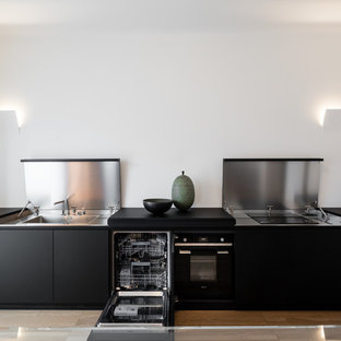 Ispirazione per una cucina moderna con lavello a vasca singola, ante nere, top in acciaio inossidabile, elettrodomestici in acciaio inossidabile, parquet chiaro, nessuna isola, pavimento marrone e top nero