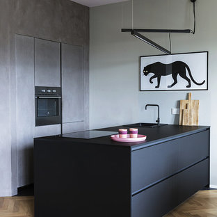 Idee per una cucina parallela design con ante nere, elettrodomestici in acciaio inossidabile, top nero, lavello da incasso, ante lisce, parquet chiaro, penisola e pavimento marrone