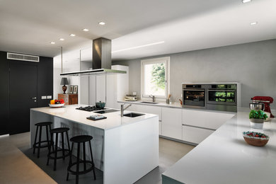Immagine di una cucina minimal con ante lisce, ante bianche, elettrodomestici in acciaio inossidabile, top bianco, lavello sottopiano, paraspruzzi grigio, pavimento in cemento e pavimento grigio