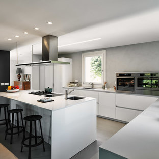 Immagine di una cucina minimal con ante lisce, ante bianche, elettrodomestici in acciaio inossidabile, top bianco, lavello sottopiano, paraspruzzi grigio, pavimento in cemento e pavimento grigio