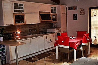 ナポリにある中くらいなシャビーシック調のおしゃれなキッチン (ダブルシンク、白いキャビネット、木材カウンター、白い調理設備、磁器タイルの床、アイランドなし、ベージュの床、茶色いキッチンカウンター) の写真