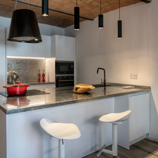 Idee per una cucina parallela minimal con lavello integrato, ante lisce, ante bianche, top in acciaio inossidabile, paraspruzzi a effetto metallico, elettrodomestici neri, pavimento in legno massello medio, penisola, pavimento marrone, top grigio e soffitto a volta
